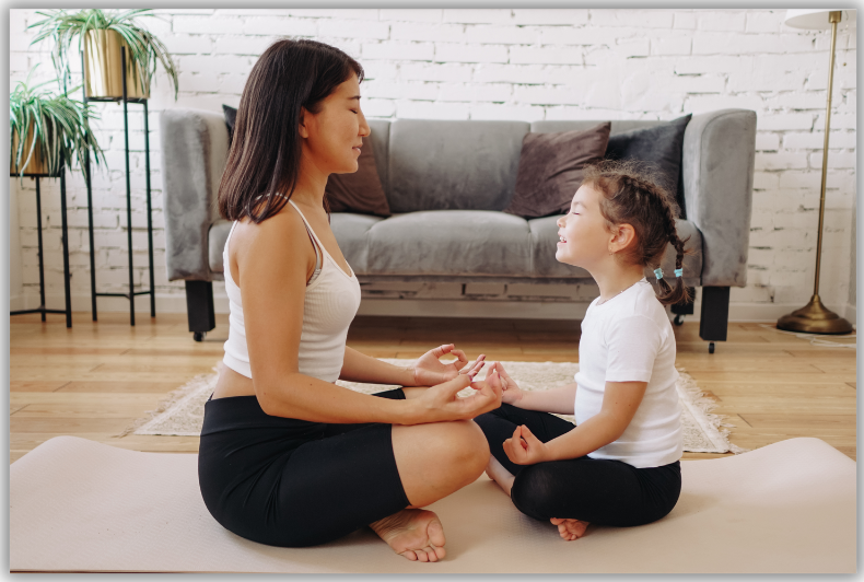 Mother and daughter meditating on a white rug in front of a gray couch.
