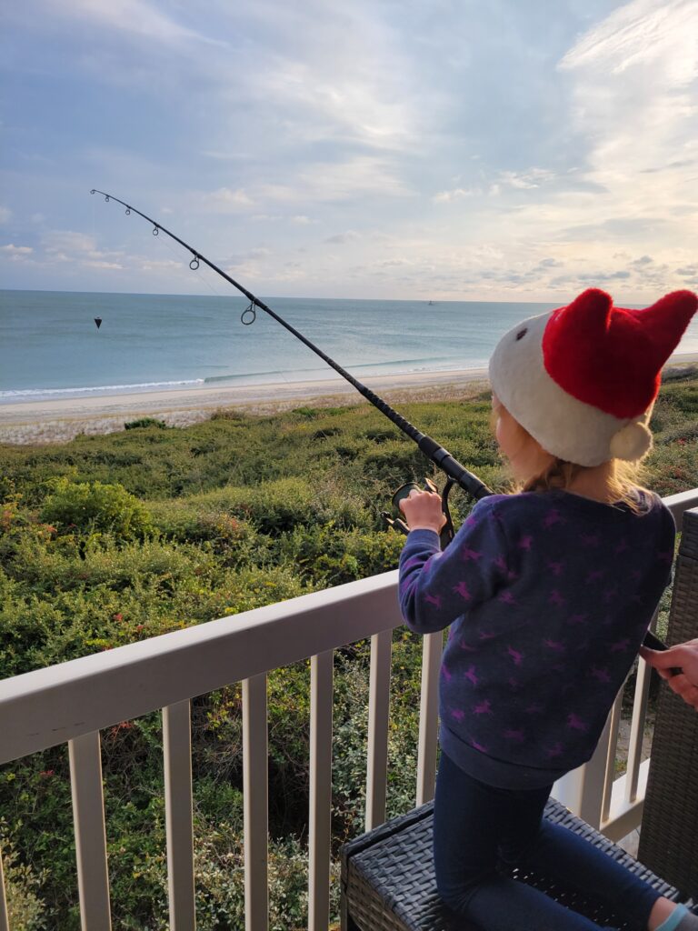 Girl fishing off of a balcony, overlooking the beach.